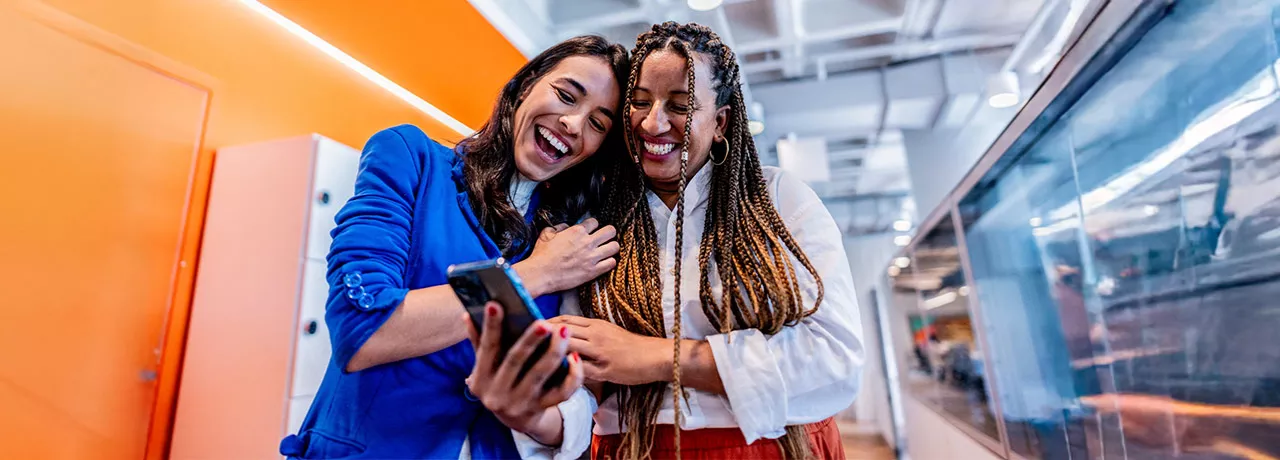 duas mulheres rindo enquanto olham algo em celular.