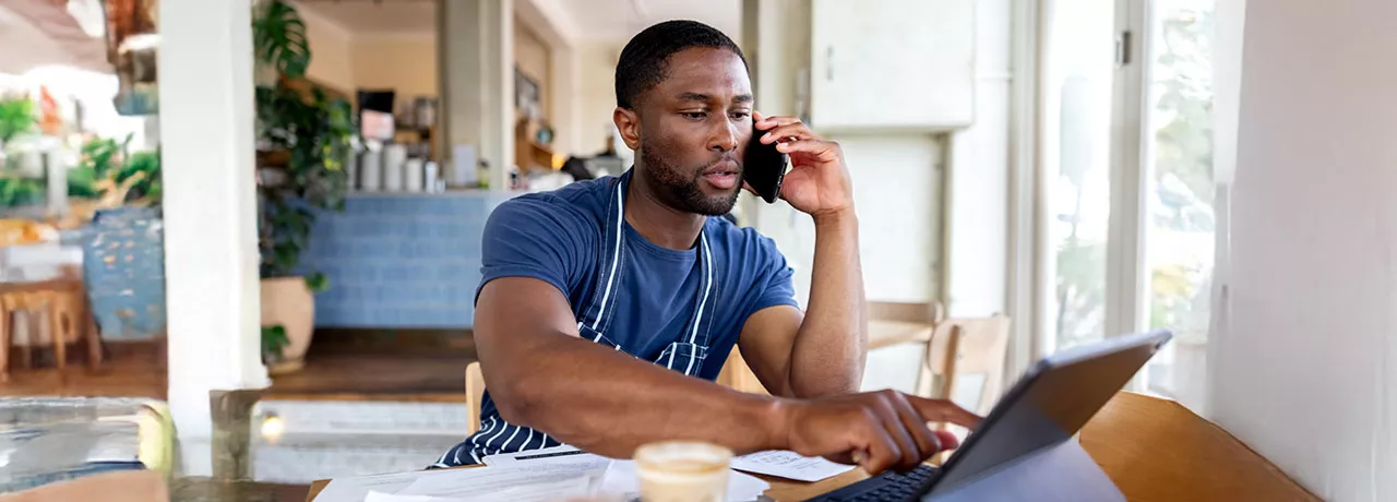 dono de empresa falando no telefone enquanto usa notebook.