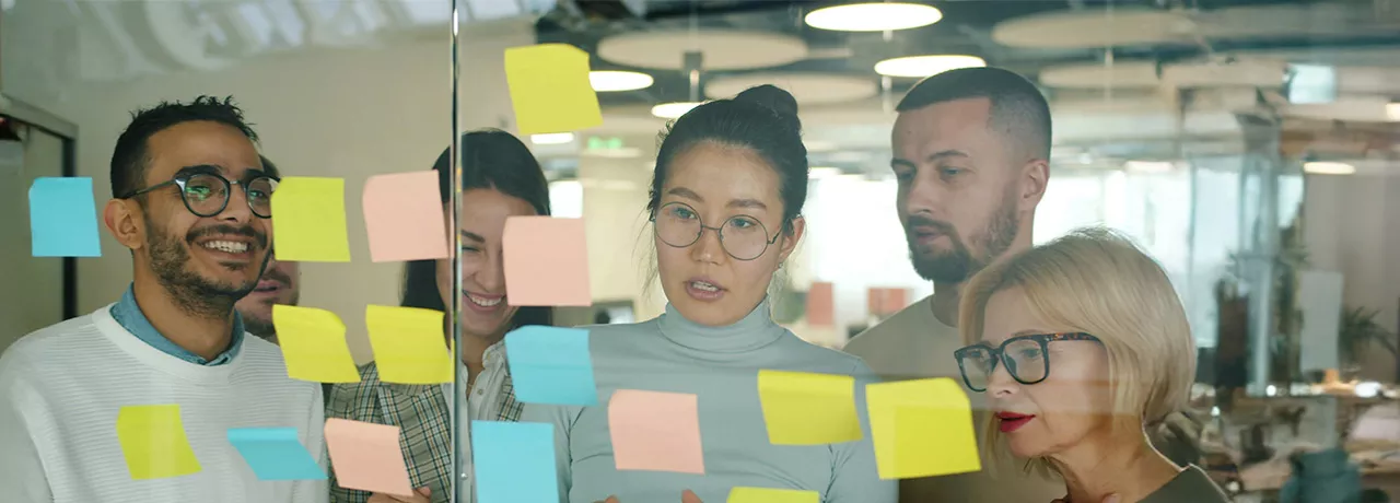 grupo de pessoas olhando para notas autoadesivas em parede de vidro.