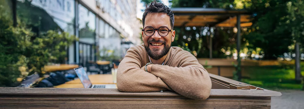 Homem sorrindo de braços cruzados no ambiente corporativo
