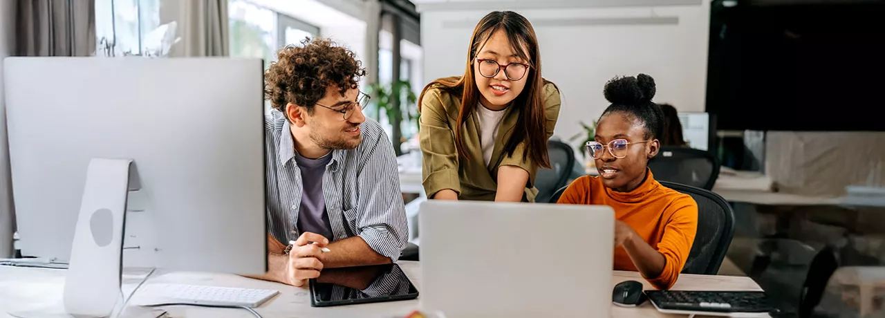 três pessoas conversando enquanto olham algo em computador.