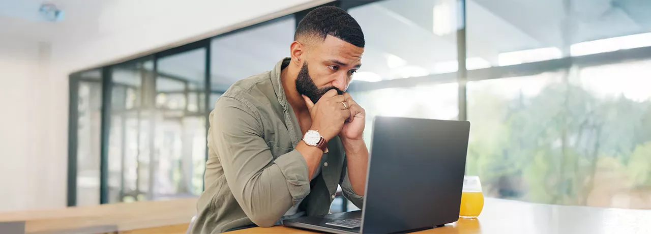 Foto mostra um homem preocupado olhando para seu notebook no escritório
