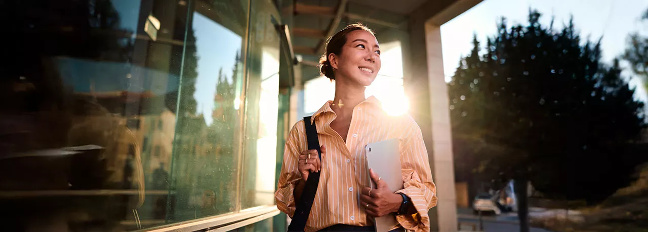 Foto de uma jovem profissional na área externa da empresa em que trabalha