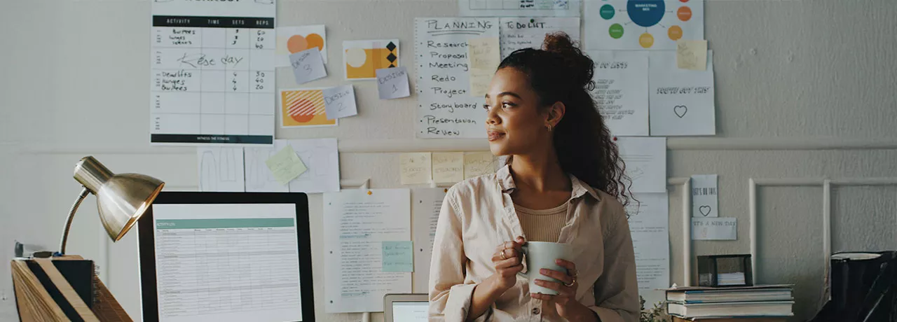 mulher segurando xícara de café em frente a uma série de papéis com planejamento estratégico.