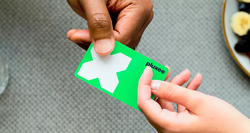 Mulher usa o cartão de benefício Pluxee para pagar uma conta. Nossos cartões são feitos com plástico reciclável!