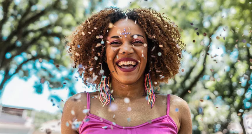 Foto mostra mulher sorridente pulando Carnaval numa praça