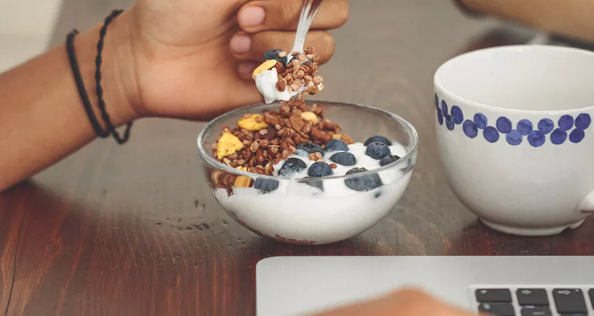 Foto mostra uma tigela de iogurte que uma pessoa está comendo durante o trabalho