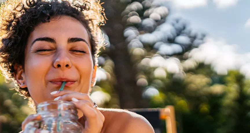 Foto mostra mulher tomando um suco em um parque