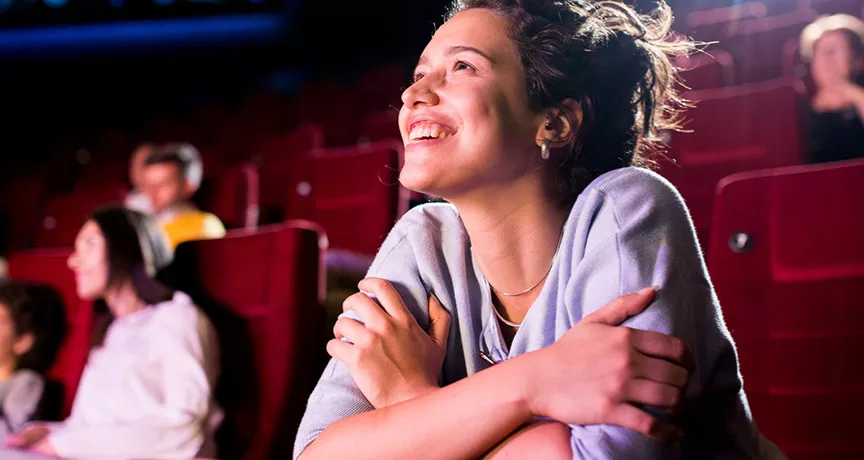 Mulher sorri e assiste com atenção a um filme no cinema