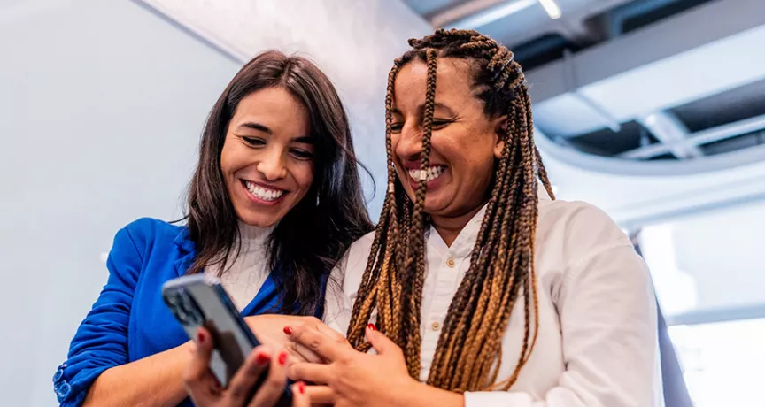 Duas amigas de trabalho conferem no celular os benefícios para funcionários que recebem da empresa