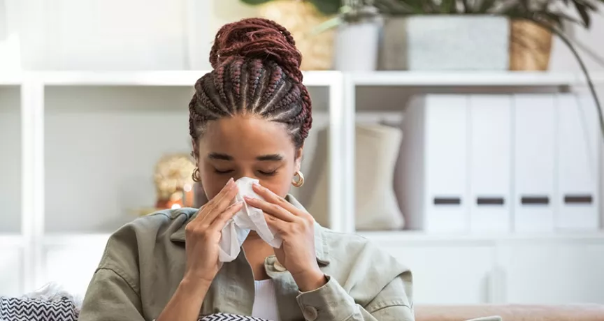 Foto mostra uma mulher assoando o nariz porque está resfriada 