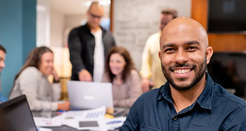 Foto mostra uma equipe de trabalho, com um homem sorrindo em destaque na frente
