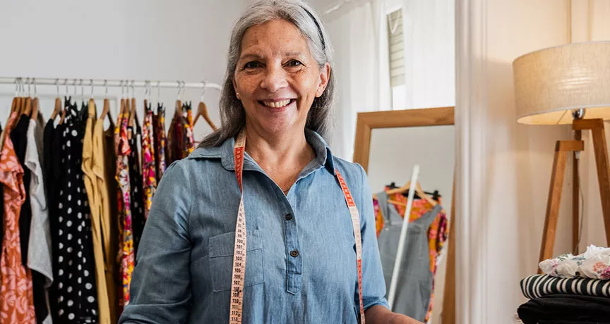 mulher grisalha dona de uma loja de roupas sorrindo para a câmera.