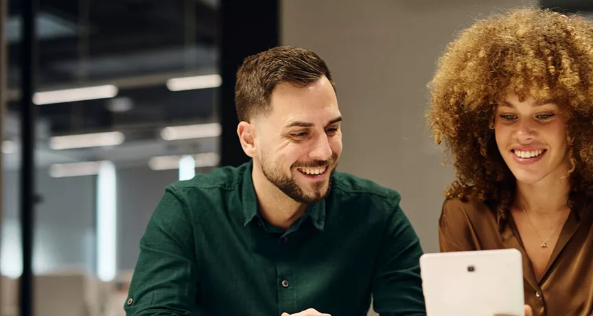 um homem e uma mulher sorrindo olhando para tablet.