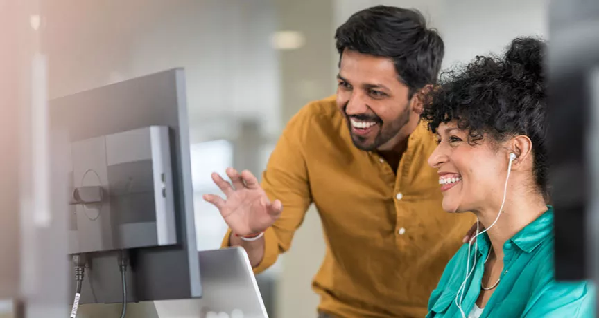 duas pessoas conversando e sorrindo em frente a um computador.