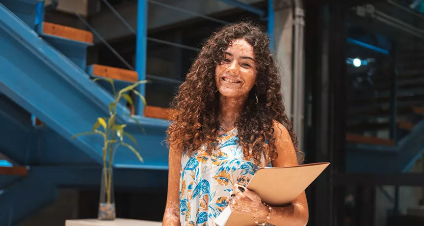 estagiária sorrindo enquanto segura documentos.