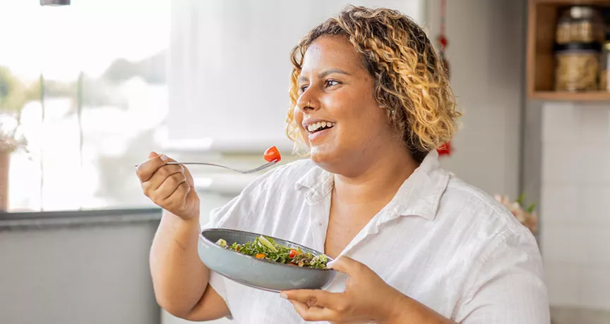 mulher comendo salada sorrindo.