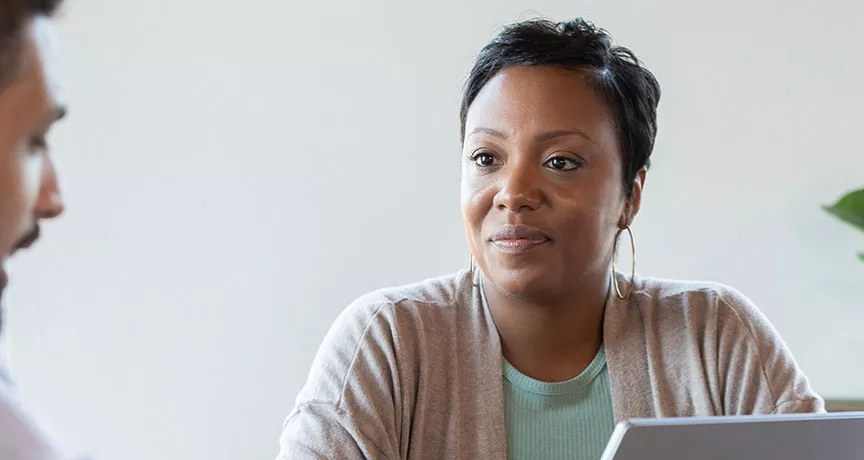 homem conversando com mulher que senta atrás de um notebook.