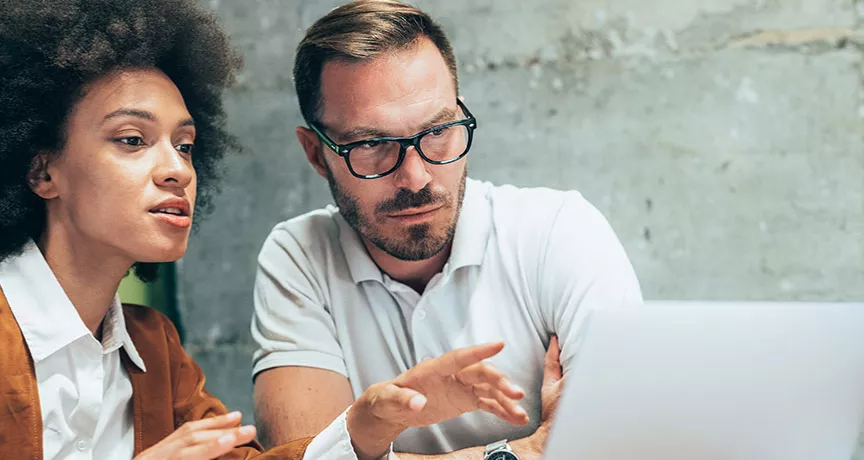 duas pessoas conversando sobre algo enquanto apontam para a tela do notebook.