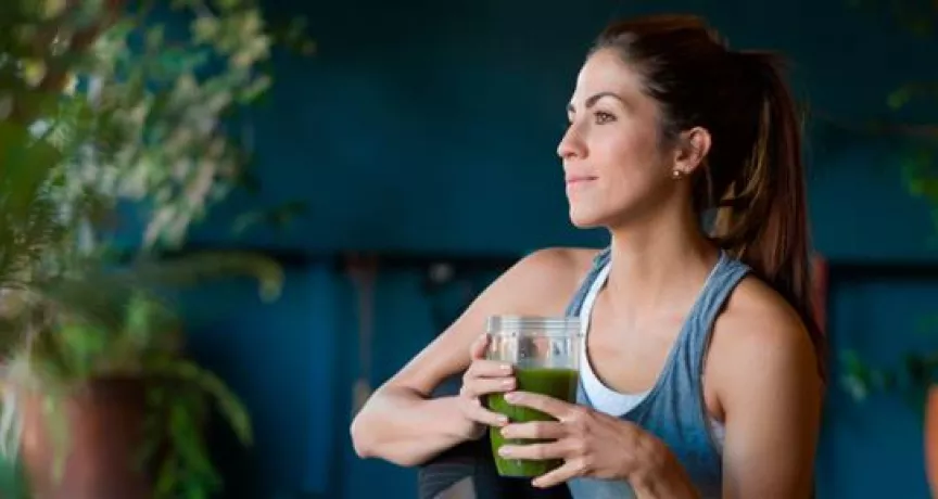 Imagem mostra uma mulher branca tomando um suco verde 