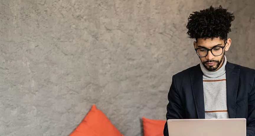 homem trabalhando com laptop no colo e semblante sério.