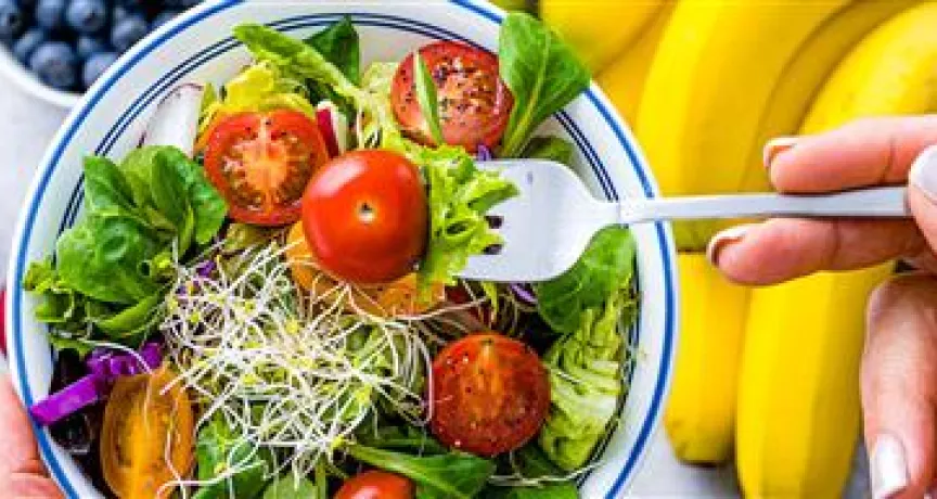Imagem mostra uma salada com tomates e frutas ao fundo