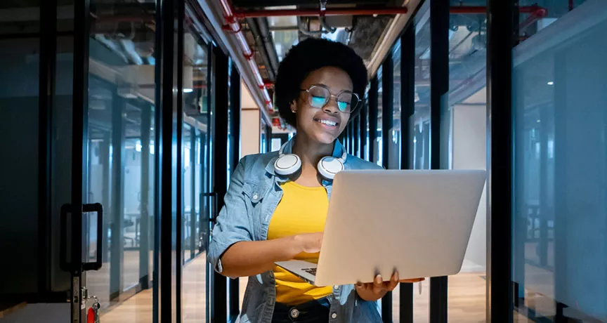 mulher sorrindo enquanto segura computador e caminha em um corredor de escritório.