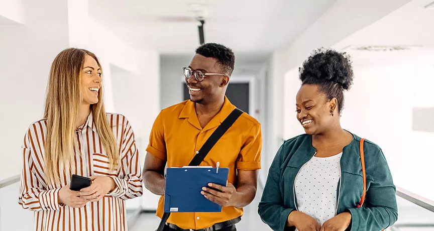 três pessoas conversando e rindo em corredor.