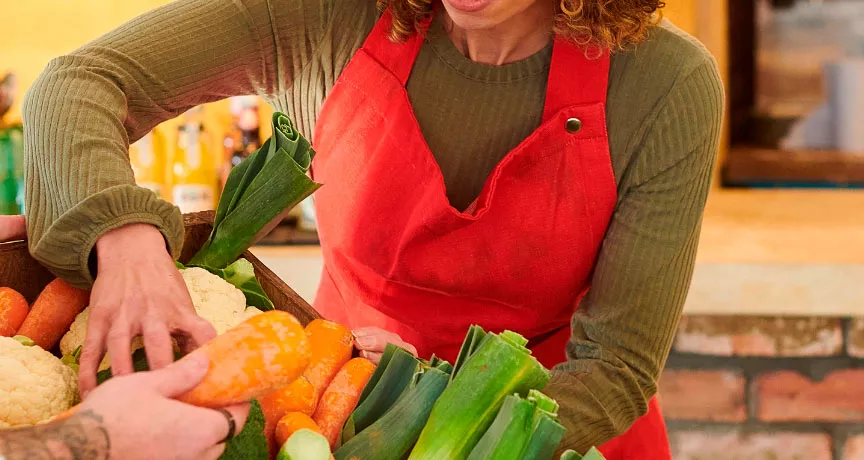 foto mostra duas pessoas mexendo em uma cesta de legumes frescos