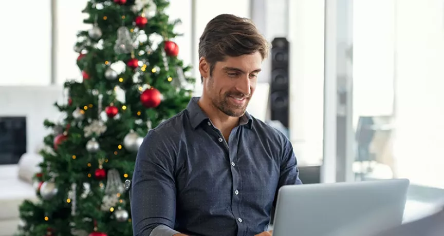 homeme trabalhando com árvore de natal atrás.