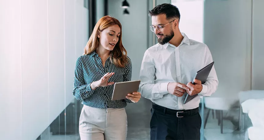 duas pessoas conversando enquanto olham dado em tablet dentro de uma empresa.