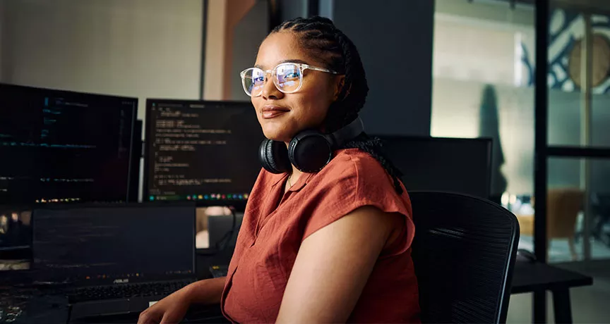 mulher sentada olhando para a câmera com monitores ao fundo.