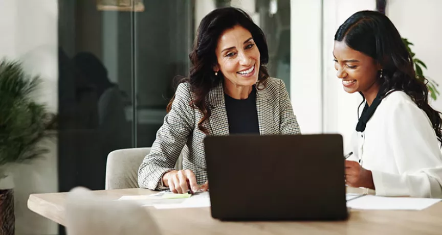 duas mulheres sorrindo enquanto conversam em frente a um notebook no escritório.