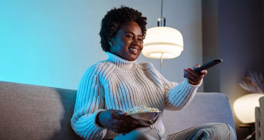 mulher em sofá segurando um balde de pipoca e controle remoto.