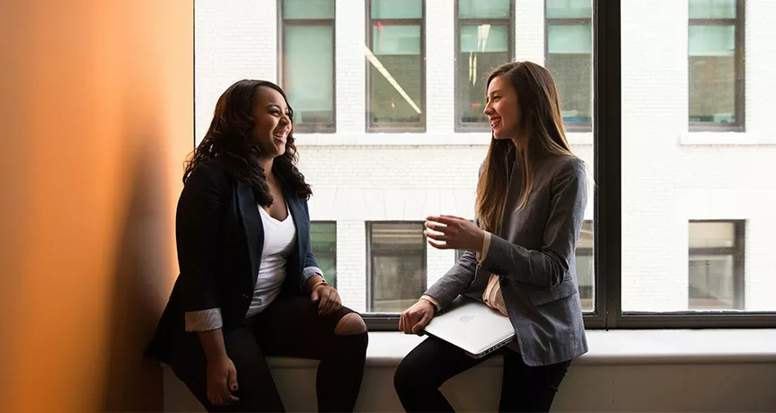 Foto mostra duas pessoas conversando em uma sala de reunião