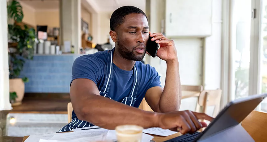 dono de empresa falando no telefone enquanto usa notebook.