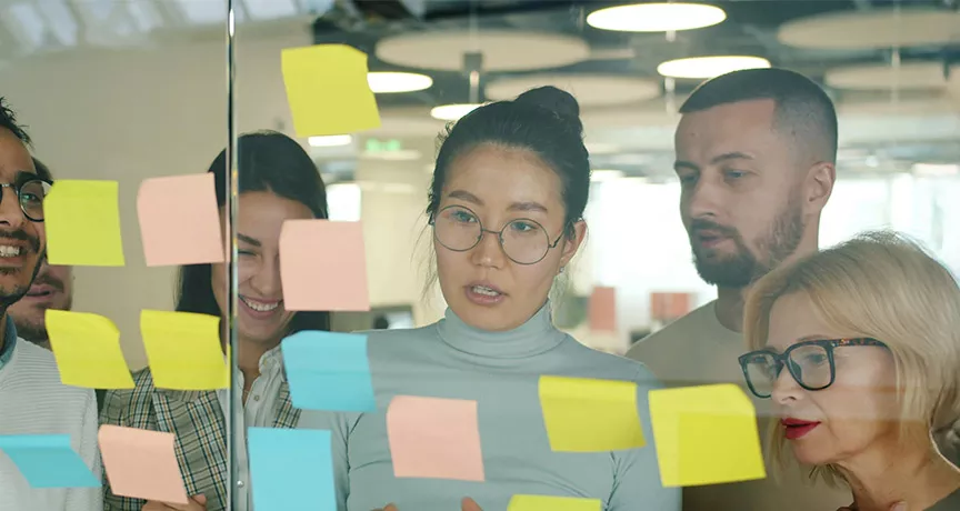 grupo de pessoas olhando para notas autoadesivas em parede de vidro.