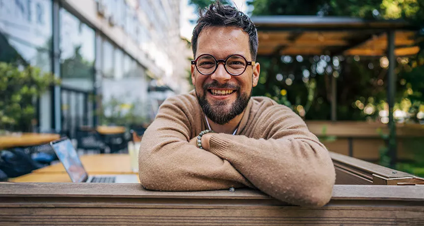 Homem sorrindo de braços cruzados no ambiente corporativo