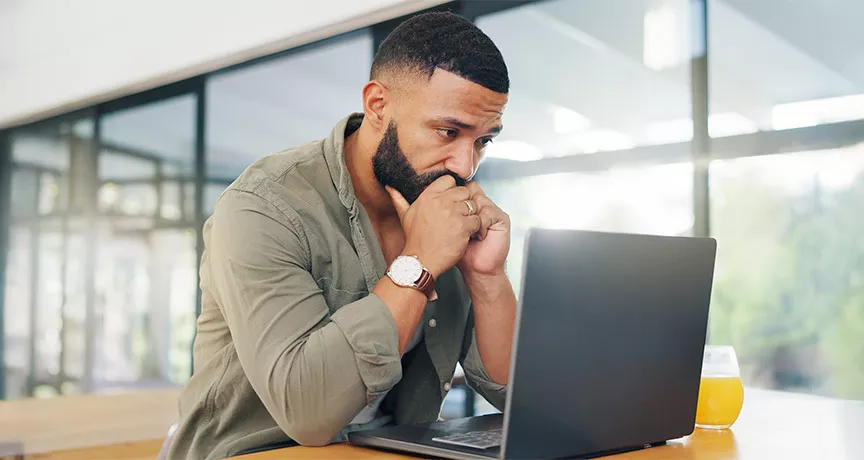 Foto mostra um homem preocupado olhando para seu notebook no escritório