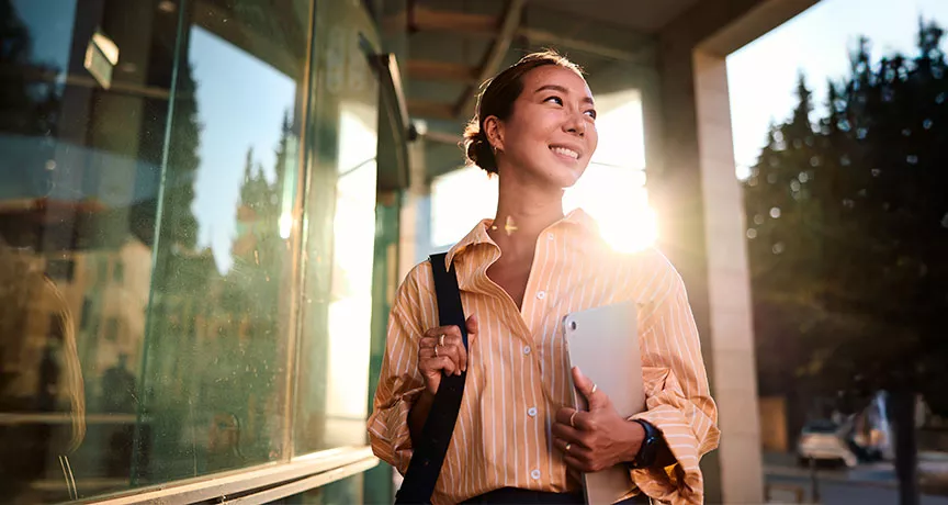 Foto de uma jovem profissional na área externa da empresa em que trabalha