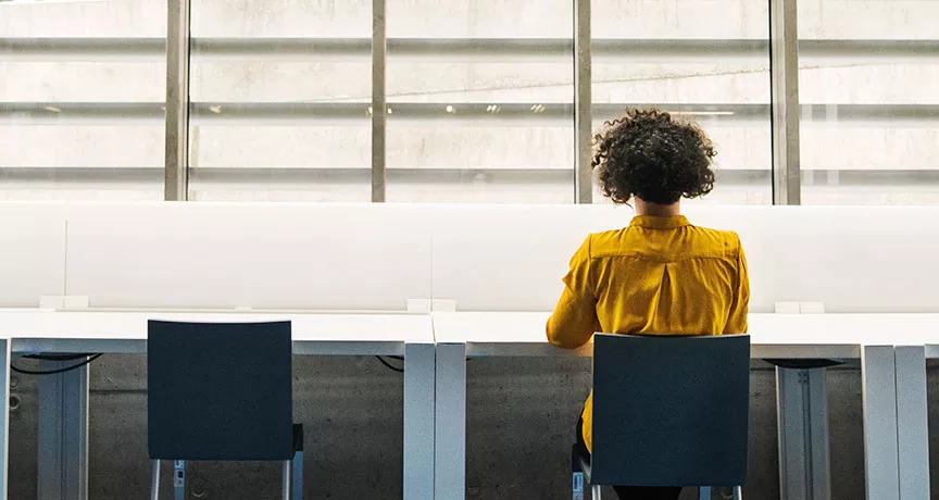 mulher trabalhando sozinha em mesa cheia de cadeiras.
