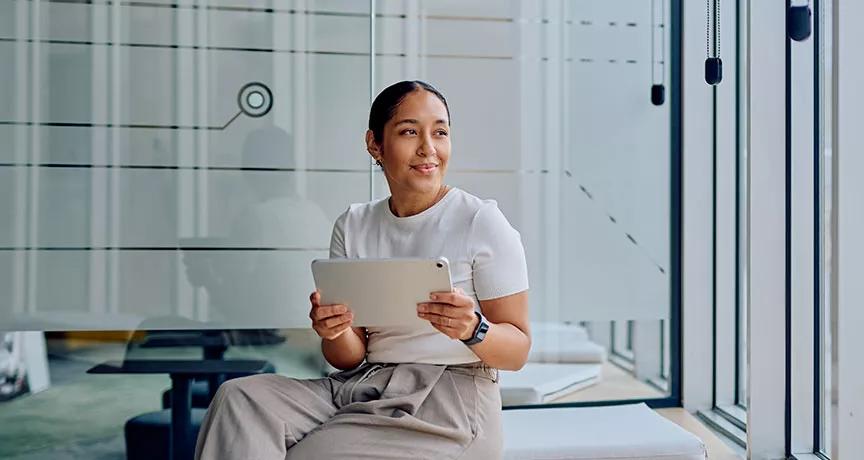 mulher segurando tablet e olhando pela janela em escritório.