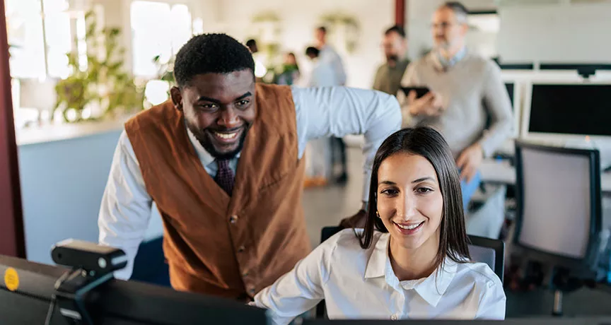 um homem e uma mulher sorrindo olhando para computador em escritório.