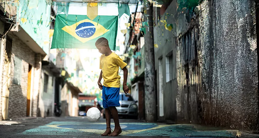 Foto mostra um menino jogando bola em uma rua enfeitada para a Copa do Mundo