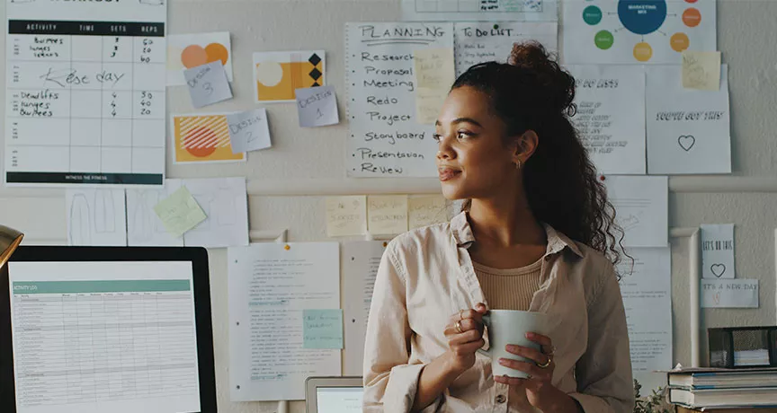 mulher segurando xícara de café em frente a uma série de papéis com planejamento estratégico.