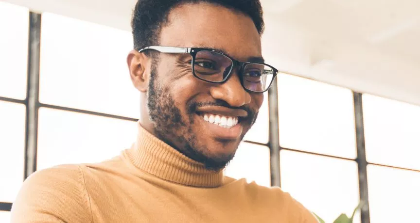 Homem negro, de camiseta amarela olhando para o notebook e sorrindo