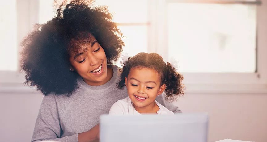 mãe e filha sorrindo enquanto olham algo no computador.