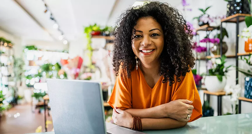 dona de floricultura sorrindo com computador.