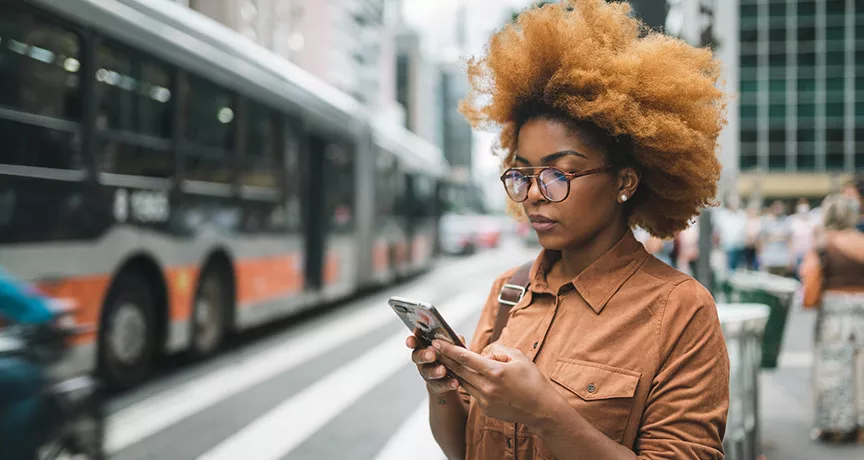 Mulher olha o celular, com um ônibus ao fundo
