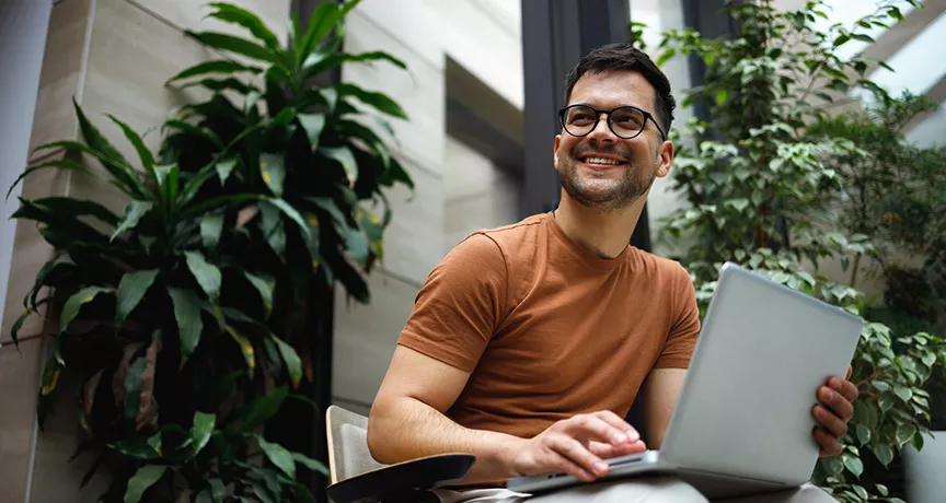 homem usando notebook no colo enquanto sorri.